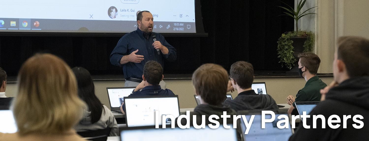 Presenter in front of room of students. Text: Industry Partners