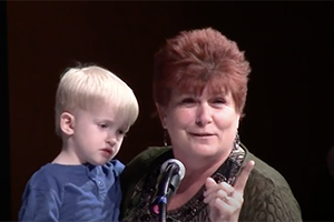Laurie Little speaks at podium while holding toddler grandson after winning award